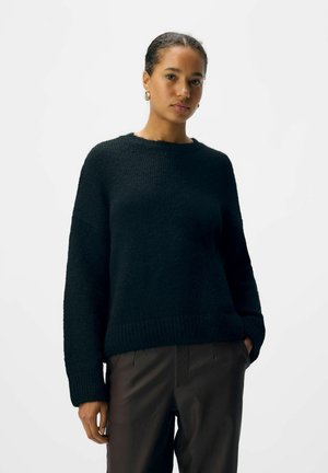 Schwarzer gestrickter Pullover mit Rundhalsausschnitt und lockerem Schnitt. Verfügt über einen gerippten Saum und Bündchen, kombiniert mit dunklen Hosen. Glatte Textur.