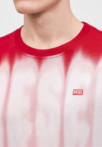 Homme portant un t-shirt tie-dye rouge et blanc Diesel avec un col rond et le logo Diesel sur la poitrine.