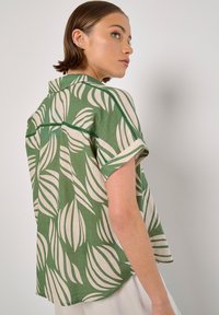 Camicia verde a maniche corte con motivo a foglia, realizzata in tessuto testurizzato, con colletto e accenti crema a contrasto lungo le cuciture.
