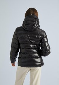 Giacca a vento nera con finitura lucida, cuciture orizzontali e cappuccio. Presenta una silhouette aderente e una texture liscia.