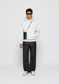 Grå hettegenser, mørke denimjeans, svart crossover-veske, solbriller og kremfargede sneakers. Avslappet passform, glatt stoff og enkelt design.
