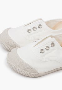 Weiße Slip-On-Schuhe aus Canvas mit runden Metallösen, Gummischutzkappen und strukturiertem Gummisohle. Weiches Obermaterial aus Stoff mit minimaler Naht.