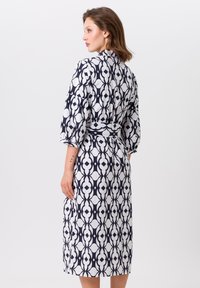 Robe à motif bleu marine et blanc avec des manches trois-quarts, une ceinture à nouer, et une coupe à hauteur des genoux présentant des formes géométriques.