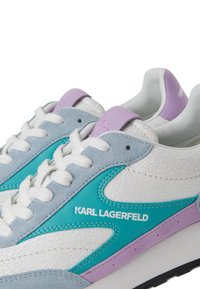 Textúrás fehér bőrből készült sportcipő, türkiz és világoslila részletekkel, valamint fehér fűzőkkel. Lapos talp jellemzi, az oldalon logóval.