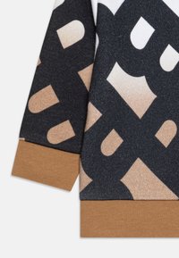 Sweatshirt noir et beige avec de grands motifs graphiques, un tissu texturé, et des poignets et ourlets côtelés brun contrastants.