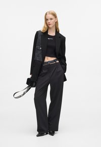 Melnā pielāgotā žakete ar denim paneļa, melns cropped tops un brīvi melni bikses. Aksesuāri ietver mazu melnu somiņu ar rakstainu siksniņu.