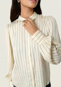 Cream-colored long-sleeve blouse with vertical blue stripes, button closure, and puff sleeves. Smooth fabric texture with a soft drape.