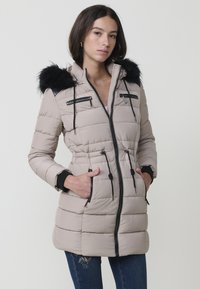 Abrigo puffer beige claro con capucha de piel sintética, cierre frontal con cremallera y dos bolsillos en el pecho con cremallera. Diseño acolchado texturizado y cinturilla ajustable.