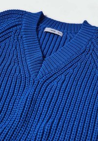 Pull en grosse maille bleu avec col en V et étiquette de marque visible "MNG" à l'intérieur du col au dos.