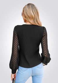 Top negro con cuerpo acanalado y mangas transparentes con patrón en zigzag y puños abullonados. Combinado con jeans de mezclilla azules.