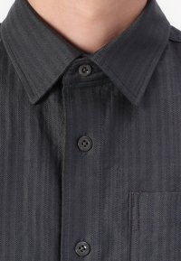 Dark gray button-up shirt in herringbone pattern, featuring a pointed collar, black buttons, and a pocket on the left side.