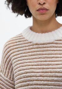 Raidallinen neulepusero, jossa vuorottelevat ruskeat ja kermaiset värit, joustava valkoinen kaulus ja pehmeä, teksturoitu pinta.