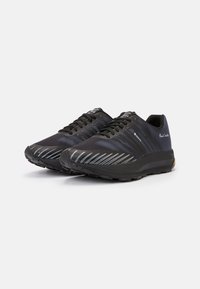 Chaussures de sport noires avec une tige texturée, présentant des rayures diagonales bleues et une semelle en caoutchouc durable pour une meilleure adhérence. Modèle à lacets.