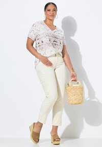 Krátký rukáv, top s véčkovým výstřihem v světlé béžové barvě se vzorem hada. Krémové kalhoty s květinovou výšivkou. Hnědé platformové podpatky a tkaná kabelka.