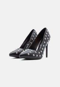 Svarte pumps med høye hæler og spisse tær, pyntet med sølvfargede nagler på overdelen. Laget av glatt skinn med blank finish.