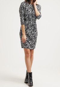 Sittande klänning i svart och vit abstrakt mönster, med trekvartslånga ärmar och draperad midja. Bärs med svarta ankelstövlar.