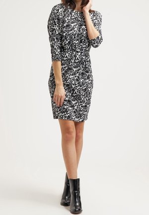 Robe ajustée en motif abstrait noir et blanc, avec des manches trois-quarts et une taille froncée. Portée avec des bottines noires. 