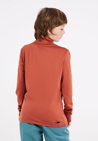 Langarm turtleneck shirt in roestoranje stof, met een gladde textuur en een gebogen zoom, gecombineerd met turkooise broek.