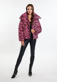 Roze luipaardprint pufferjack met oversized kraag, ritsluiting en elastische manchetten, gecombineerd met zwarte strakke leggings en lakleren enkellaarsjes.