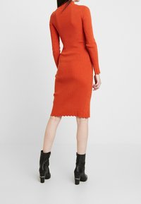 Ribbad orange klänning med en figursydd form, långa ärmar och scallopdetalj i fållen. Bärs med svarta ankelboots med en kraftig klack.