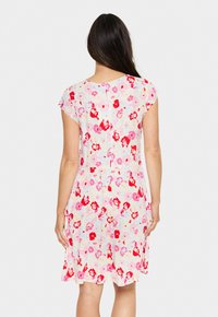 Robe florale en tissu léger, avec un fond pastel et des fleurs rouges et roses, manches courtes et coupe ample.