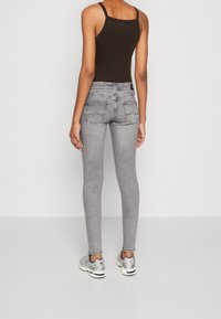 Jeans ajustados grises con una cintura de bajo ajuste, que presentan una tela suave y ligeramente texturizada, además de dos bolsillos traseros con detalles de costura en zigzag.