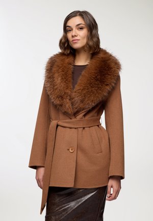 Cappotto di lana marrone con un ampio colletto di pelliccia, vita con cintura, grande bottone frontale e maniche larghe. Una gonna marrone lucida è visibile sotto.