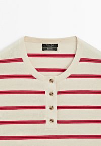 Kremowa bawełniana koszula w czerwone poziome paski, o okrągłym dekolcie i czterech brązowych guzikach na przedniej listwie.