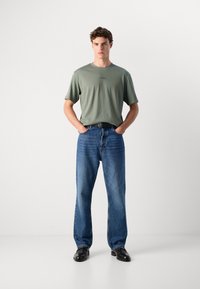 Olivengrønt t-shirt, afslappet pasform med lille logo detalje. Blå lige ben jeans, medium vask med subtil falming. Sorte sko, minimalistisk design.