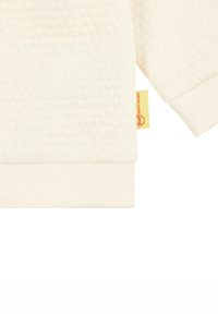 Sweatshirt de couleur crème avec un motif texturé et des poignets côtes. Présente une petite étiquette de marque jaune sur l'ourlet latéral.