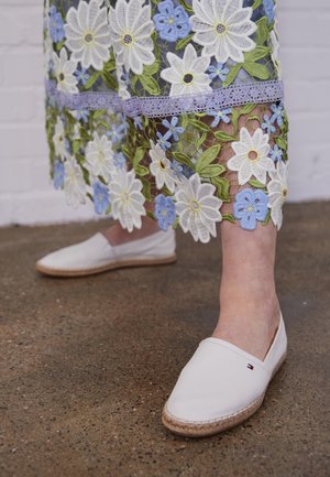 White espadrilles with a canvas upper and braided jute sole. The dress features colorful floral embroidery with green, white, and blue elements.