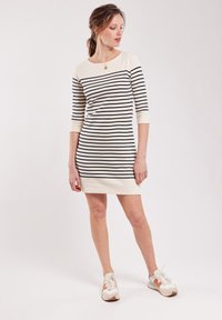 Vestito a righe con maniche a tre quarti, sfondo crema e righe blu navy. Tessuto morbido, lungo fino al ginocchio, abbinato a scarpe sportive.