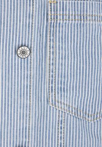 Tela a rayas azul claro con rayas verticales blancas, que presenta un botón de metal a presión etiquetado "JEANS" y un pequeño bolsillo.