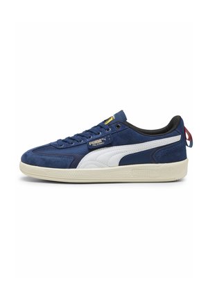 Blå ruskinds sneaker med hvide accenter, snøreoplukning, rund tå, gummisål, prydet med et logo-tag på tungen og en rød hælflap.