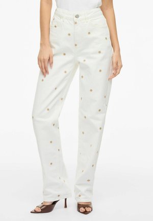 Hvide højtaljede, lige jeans med lille guldbroderet stjerne, båret med brune åbne hæle og en hvid top.