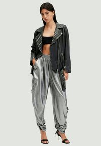 Black leather biker jacket with studded collar, paired with shiny silver cargo pants featuring pockets and gathered ankles. Stiletto heels.