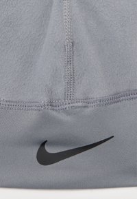 Pilkos pūkinės medžiagos audinys su sklandžia tekstūra ir matomomis siūlėmis. Yra ryškiai išryškintas juodas Nike logotipas.