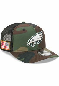 Camouflage-Cap mit grün-braunem Muster, weißem Adler-Logo auf der Vorderseite, schwarzem Netzrücken und amerikanischer Flaggenapplikation an der Seite.