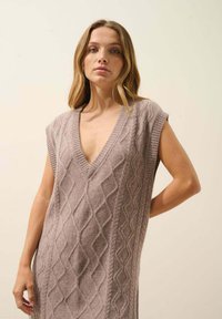 Dzianinowa sukienka bez rękawów w delikatnym, jasnym odcieniu mauve, z głębokim dekoltem w kształcie litery V, z diamentowym wzorem w warkocze i prążkowanymi detalami na krawędziach.