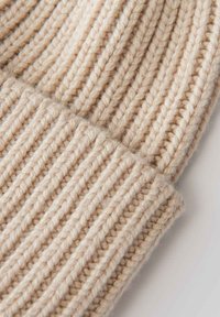 Sciarpa in maglia color beige caratterizzata da un motivo a coste texturizzato, realizzata in filato morbido con cuciture visibili e una superficie leggermente pelosa.