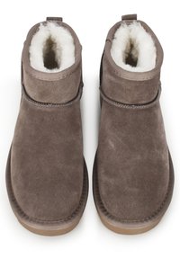 Botas de ante marrón hasta el tobillo con puntera redondeada, suave forro interior y suela de goma plana. Presentan una costura bordada y un tirador en la parte posterior.