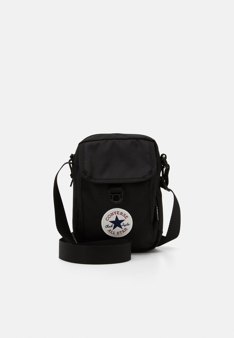 Černá látková taška přes rameno s klopou a zipovým uzávěrem. Obsahuje kulatou nášivku s logem "Converse All Star". Nastavitelný popruh, kompaktní design.