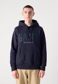 Felpa navy con polsini e bordo a coste, dotata di tasca a marsupio sulla parte frontale. Scritta "GANT New Haven, Ct." in lettere ricamate colorate.