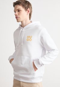 Felpa bianca con tasca frontale a marsupio, coulisse regolabile e logo giallo "HUGO". Tessuto liscio, orlo e polsini a coste.
