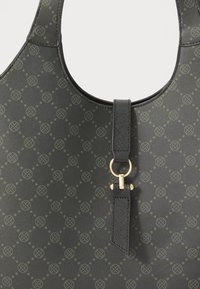 Black patterned tote bag featuring a textured surface, circular motifs, a gold-tone hardware ring, and a flat strap with an accent detail.