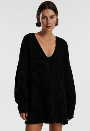 Zwarte gebreide pullover jurk met een diepe V-halslijn en losse, lange mouwen. Voorzien van een geribbeld patroon en een relaxte pasvorm.