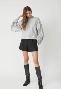 Grauer übergroßer Sweatshirt mit Fransenverzierung an den Ärmeln, kombiniert mit schwarzen Shorts und kniehohen schwarzen Stiefeln. Einfaches, lässiges Design.