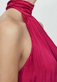 Abito halter fucsia con pieghe verticali, tessuto morbido e scollatura arricciata. Dettagli in primo piano della spalla e della scollatura.