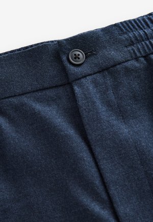 Primer plano de la cintura de unos pantalones azul oscuro con un botón y una sección elástica, mostrando costuras visibles y textura de la tela.