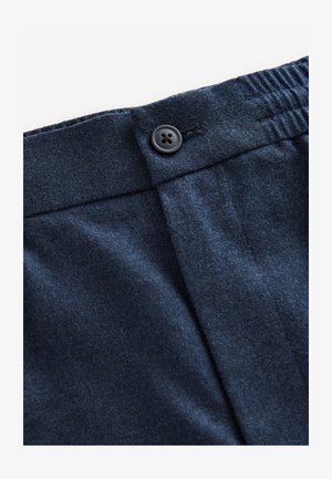 Primer plano de la cintura de unos pantalones azul oscuro con un botón y una sección elástica, mostrando costuras visibles y textura de la tela.